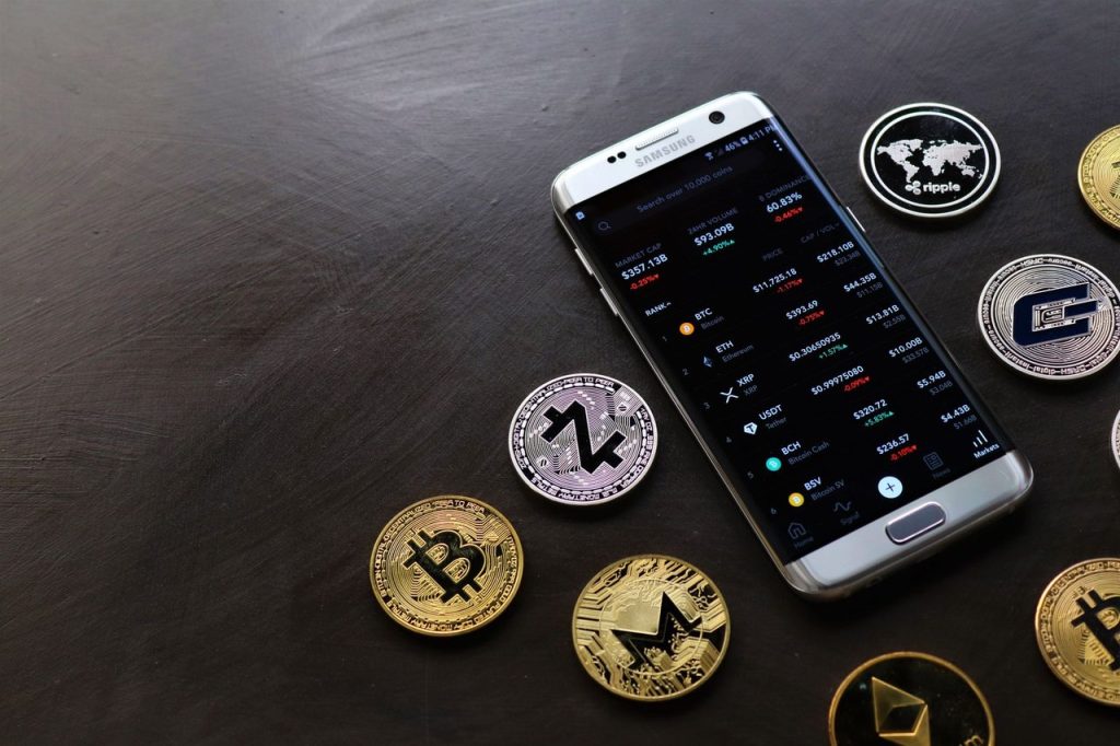 Moedas de criptomoedas ao lado de um smartphone com uma plataforma de negociação digital