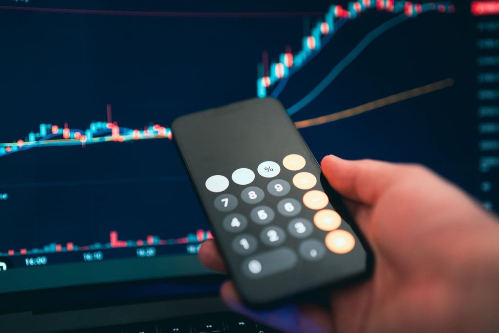 Smartphone exibindo uma calculadora sobre um gráfico financeiro.