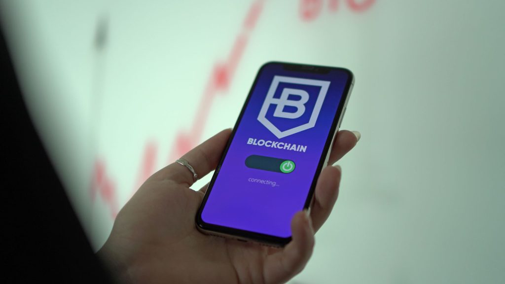 Mão segura um smartphone que exibe uma carteira digital de criptomoedas baseada em blockchain.